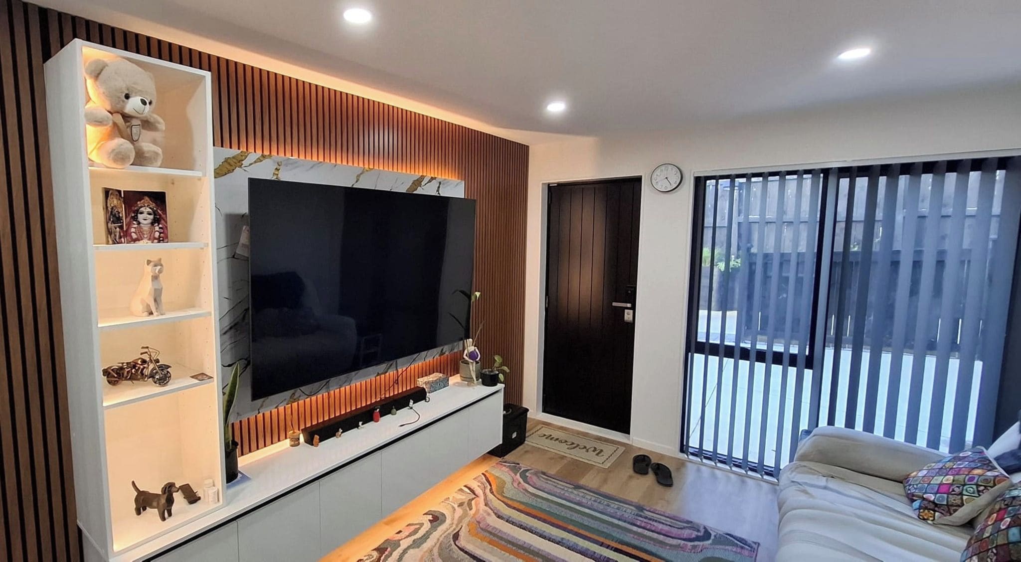 A modern living room with a large flat-screen TV, a sofa, a coffee table, and a window with blinds.