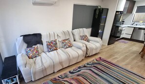 Uma sala de estar moderna com sofá, tapete estampado e área de cozinha ao fundo.