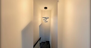 Eine enge Treppe mit einer modernen Leuchte und einem an der Wand befestigten Schild.