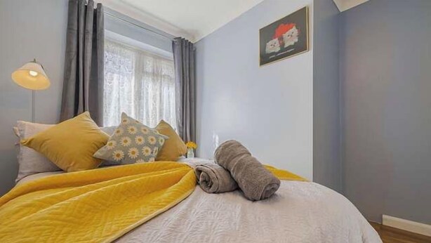 Un dormitorio con cama, almohadas, una manta, una lámpara y una ventana con cortinas.
