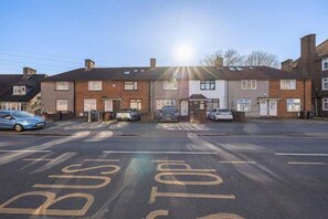 Une rue résidentielle bordée de maisons, avec des voitures garées et un ciel dégagé.
