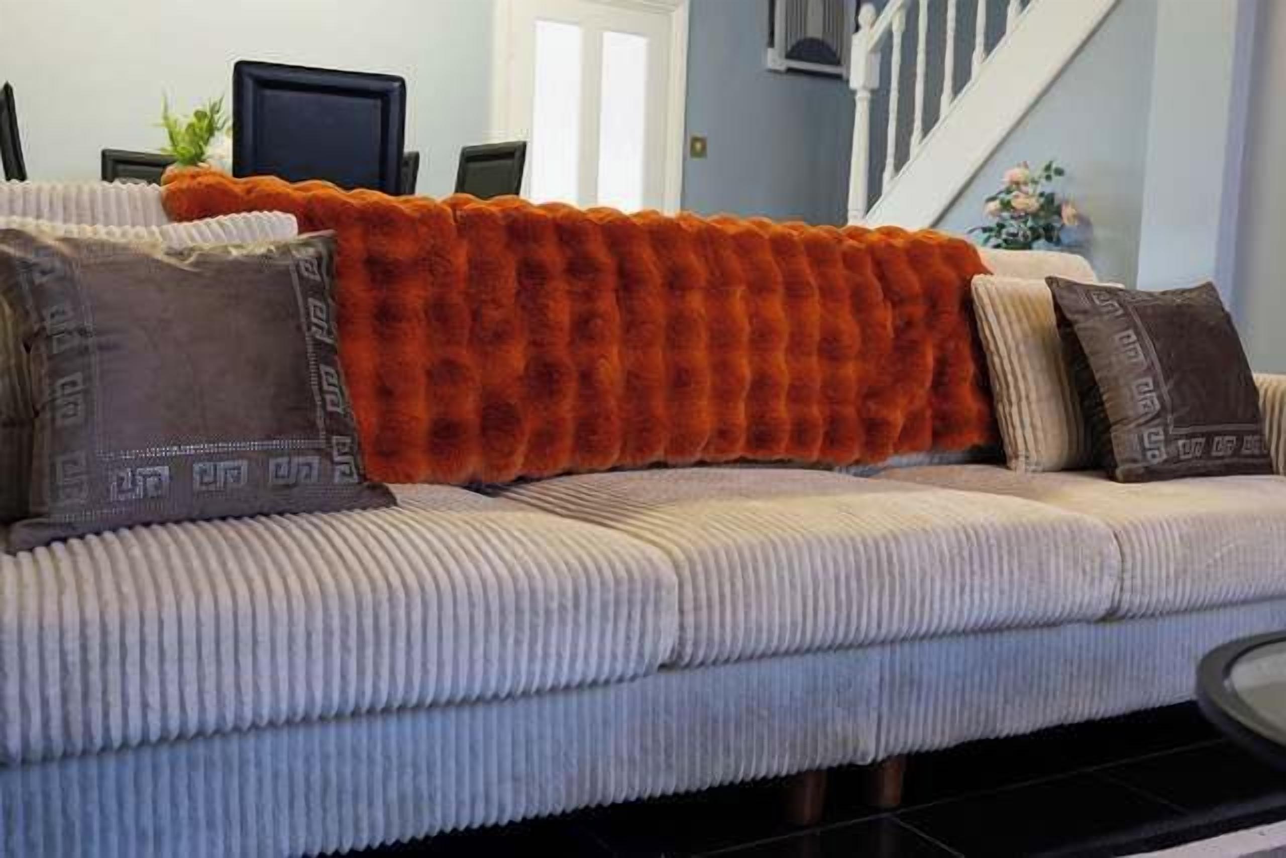 Un canapé agrémenté d’un plaid orange à texture, de coussins à motifs et d’un coussin aux tons neutres.