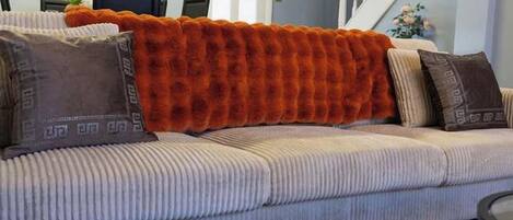 Un canapé agrémenté d’un plaid orange à texture, de coussins à motifs et d’un coussin aux tons neutres.