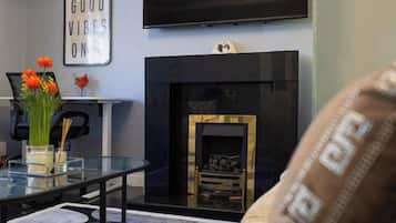A living room with a fireplace, a television mounted on the wall, and a glass table with flowers.