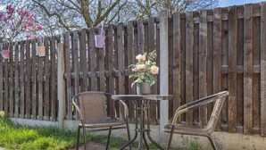 Un patio con dos sillas, una mesa, una valla de madera y una maceta con flores.