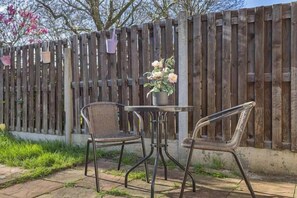 Une terrasse avec deux chaises et une table, une clôture en bois et un pot de fleurs.