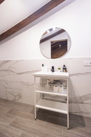 A bathroom with a white vanity, a round mirror, and marble-patterned walls.