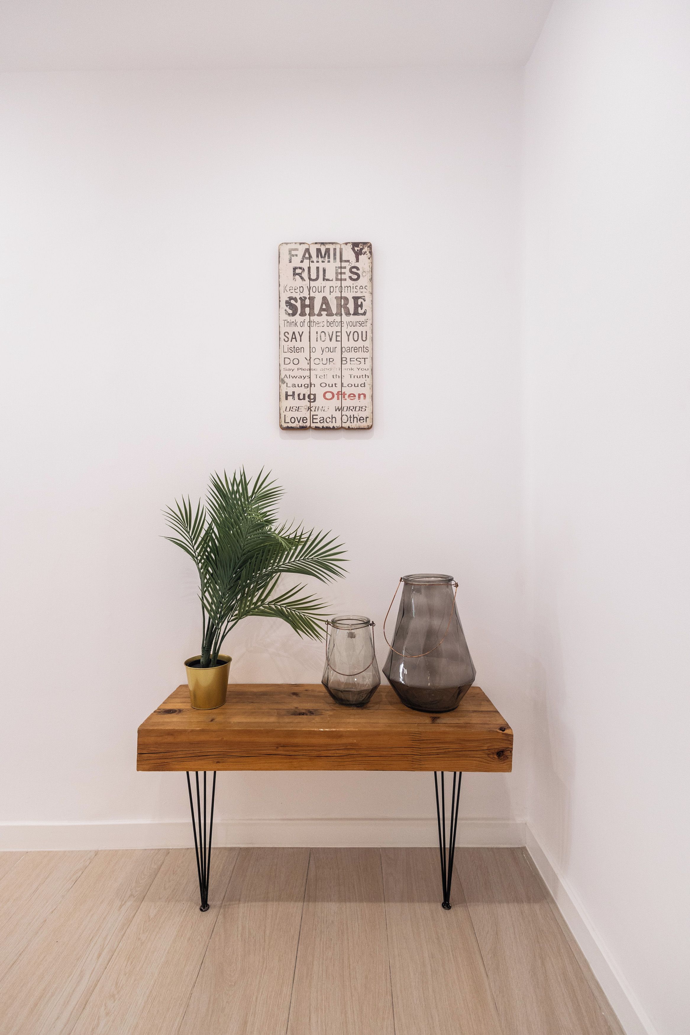 A wooden table with a potted plant and two glass jars, against a plain wall with a family rules poster.