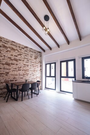 Ein geräumiger Raum mit Backsteinwand, einem Holzespeisetisch mit Stühlen und einer Küchenzeile inklusive Schränke und Spüle.