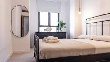 Een moderne slaapkamer met een zwart metalen bed, een ronde spiegel en een nachtkastje met een lamp.
