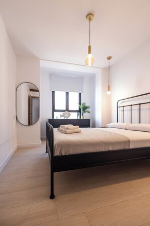 Ein modernes Schlafzimmer mit einem schwarzen Metallbettgestell, einem runden Spiegel und einem Nachttisch mit Lampe.