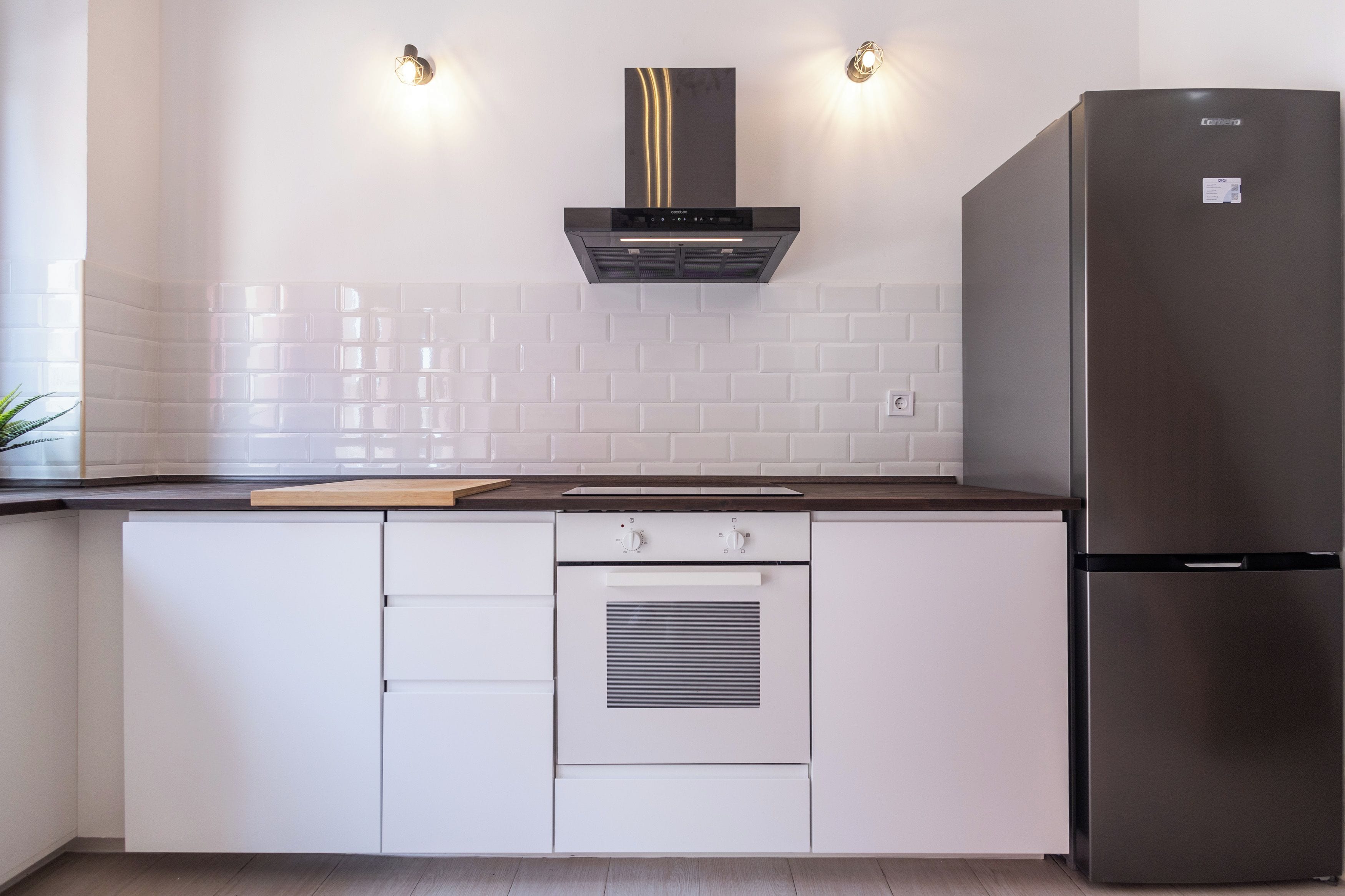 A kitchen with white cabinets, a stainless steel refrigerator, a built-in oven, and a range hood.