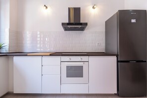 A kitchen with white cabinets, a stainless steel refrigerator, a built-in oven, and a range hood.