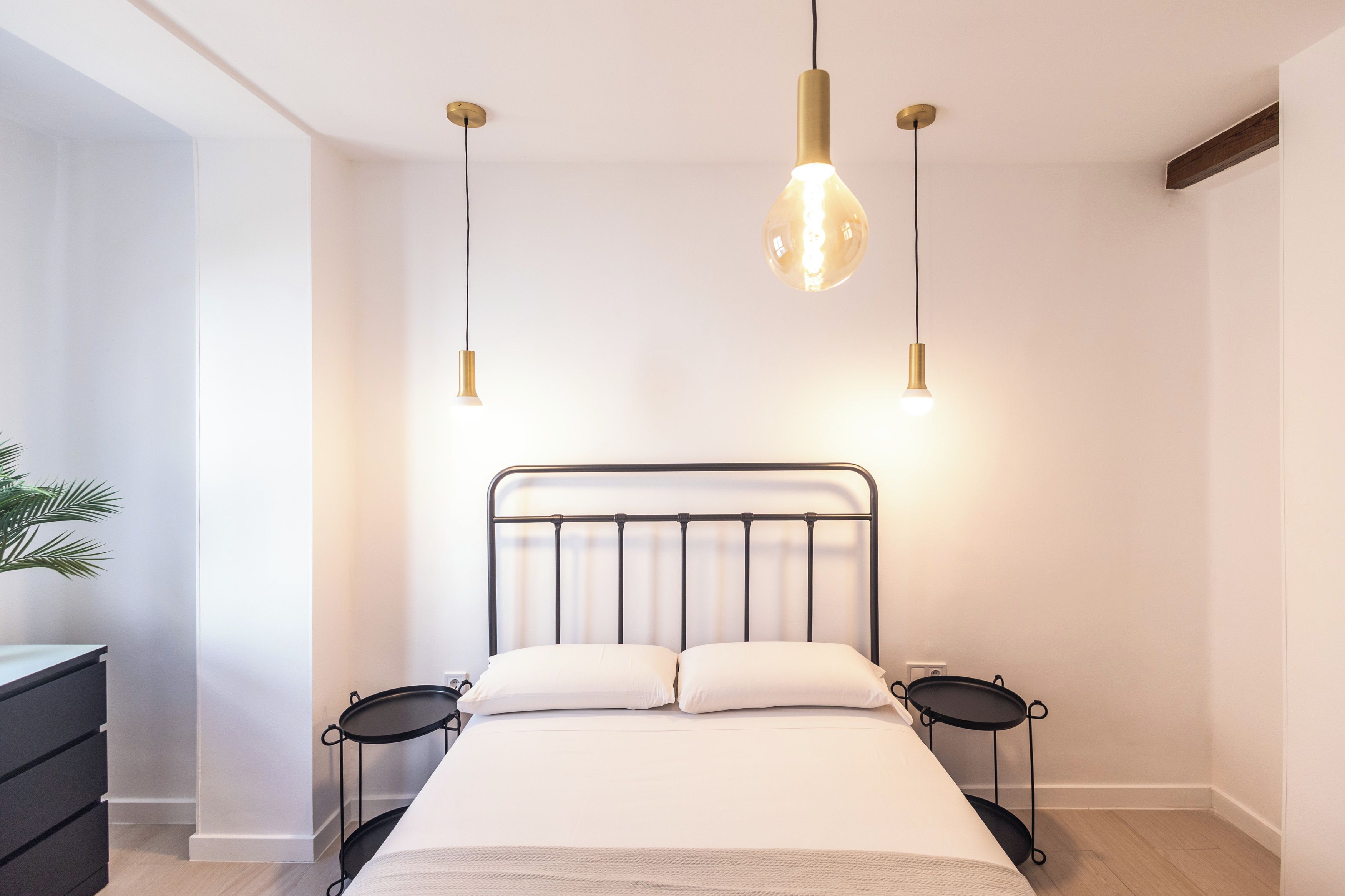 Quarto com cama, mesas de cabeceira e luminárias pendentes.