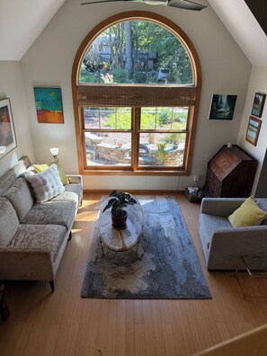 A cozy living room with a large arched window, a stone fireplace, and a potted plant on a coffee table. - The ‘Little House’ in Black Mountain (Black Mountain)