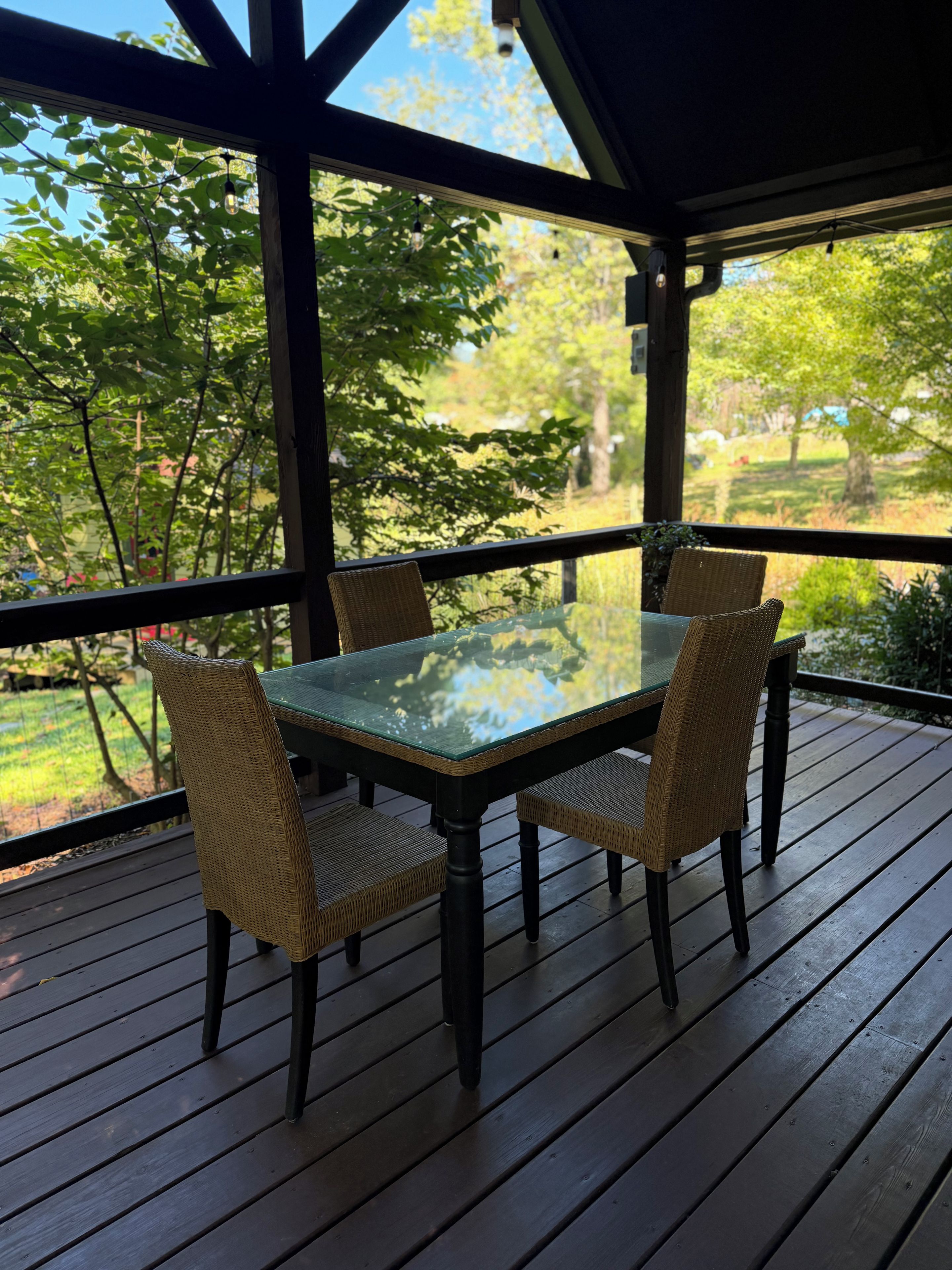 Een overdekt terras met een tafel met glazen blad en rieten stoelen.