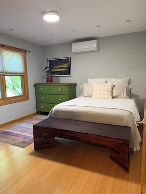 Une chambre à coucher avec un lit, une commode, une fenêtre avec des stores, un climatiseur et un tableau accroché au mur.