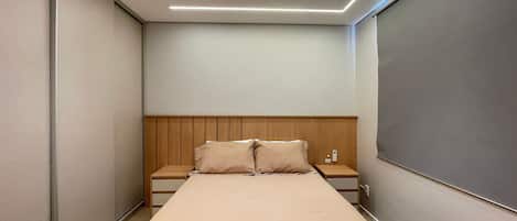 A narrow hotel room with a single bed, a wooden headboard, a bedside table with a phone, and a wall-mounted light fixture.