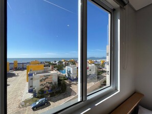 A view from a window overlooking a coastal area with buildings, a clear sky, and a distant shoreline. - Solarium Beach Club -Apartamento T1.503 (Itapoá)