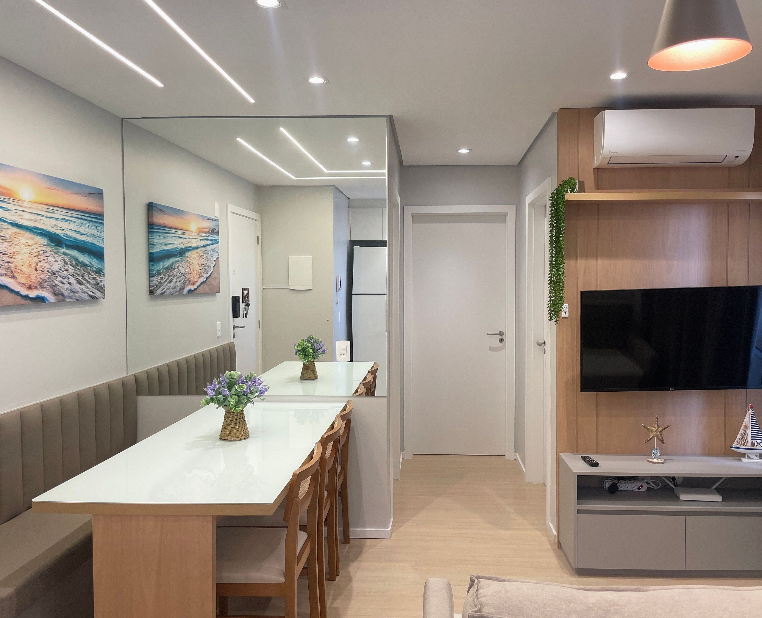 A modern kitchen with a built-in oven, a dining area with a long table and chairs, and a television mounted on a wooden cabinet.