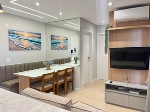 A modern living room with a dining area, a flat-screen TV, and artwork on the walls. - Solarium Beach Club -Apartamento T1.503 (Itapoá)
