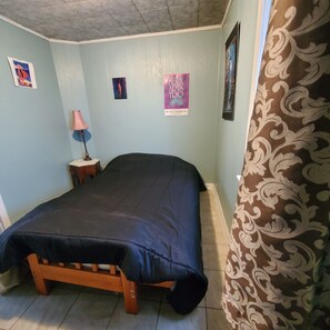 Un dormitorio con cama, mesita de noche, lámpara y carteles en la pared.
