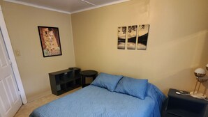 Een slaapkamer met een bed, nachtkastje, bureau en wanddecoratie.