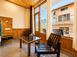A wooden interior with a table and chairs, a bench, and a window with a view of a building and mountains.