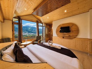 A hotel room with a large bed, a TV mounted on a wooden wall, and a view of a mountainous landscape. - The Heaven Paradise Manali (Manali)