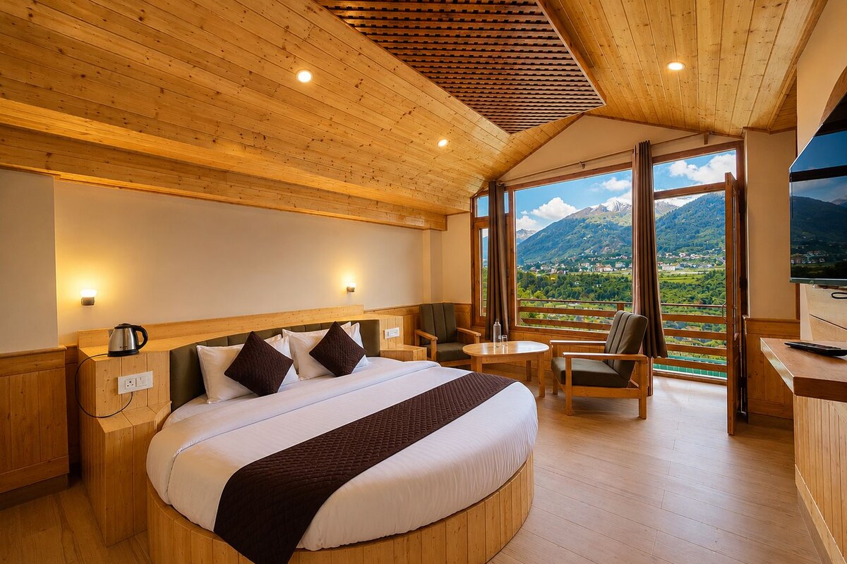A hotel room with a large bed, a TV, a seating area, and a view of mountains.