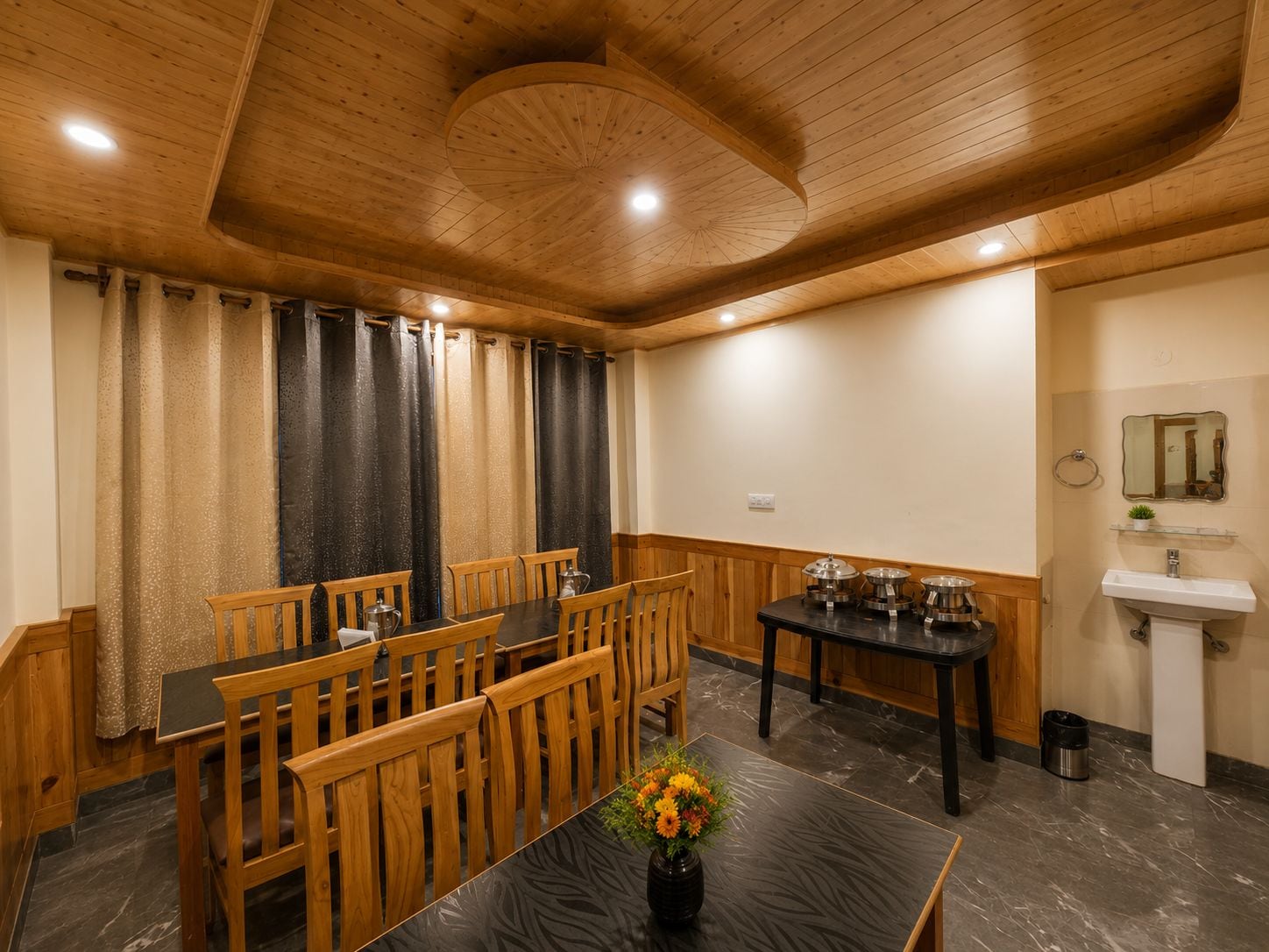 Uma sala de jantar com mobiliário de madeira, uma mesa com um vaso de flores e uma pia fixa na parede.