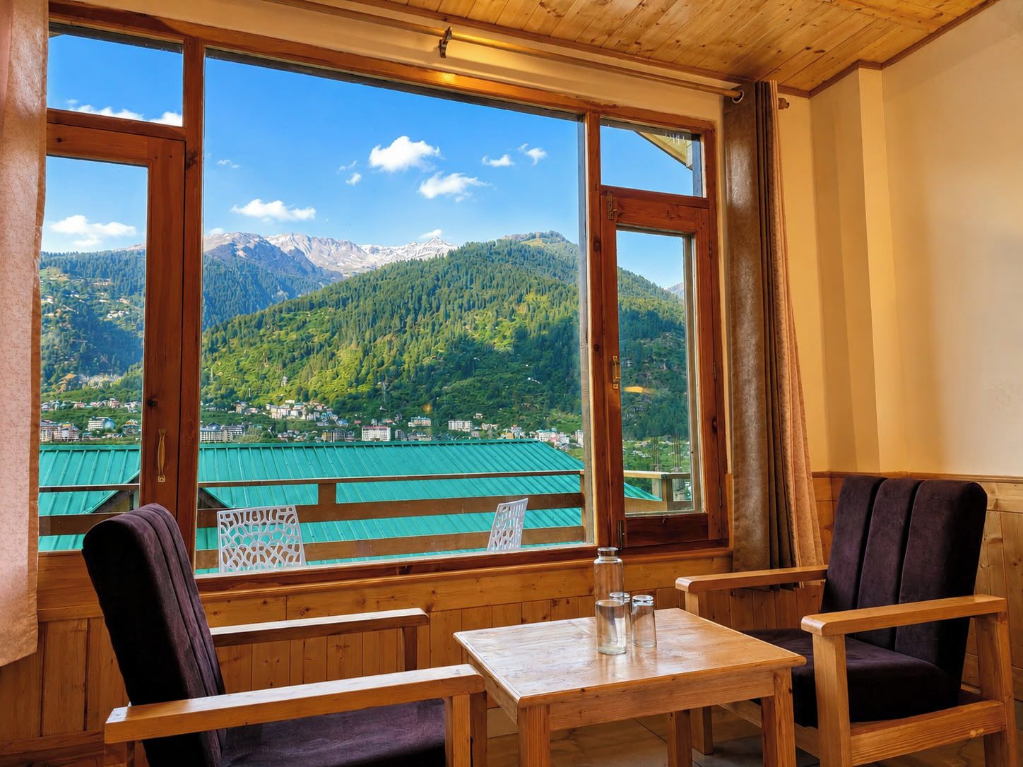 A room with wooden furniture, a table, and large windows offering a mountain view.