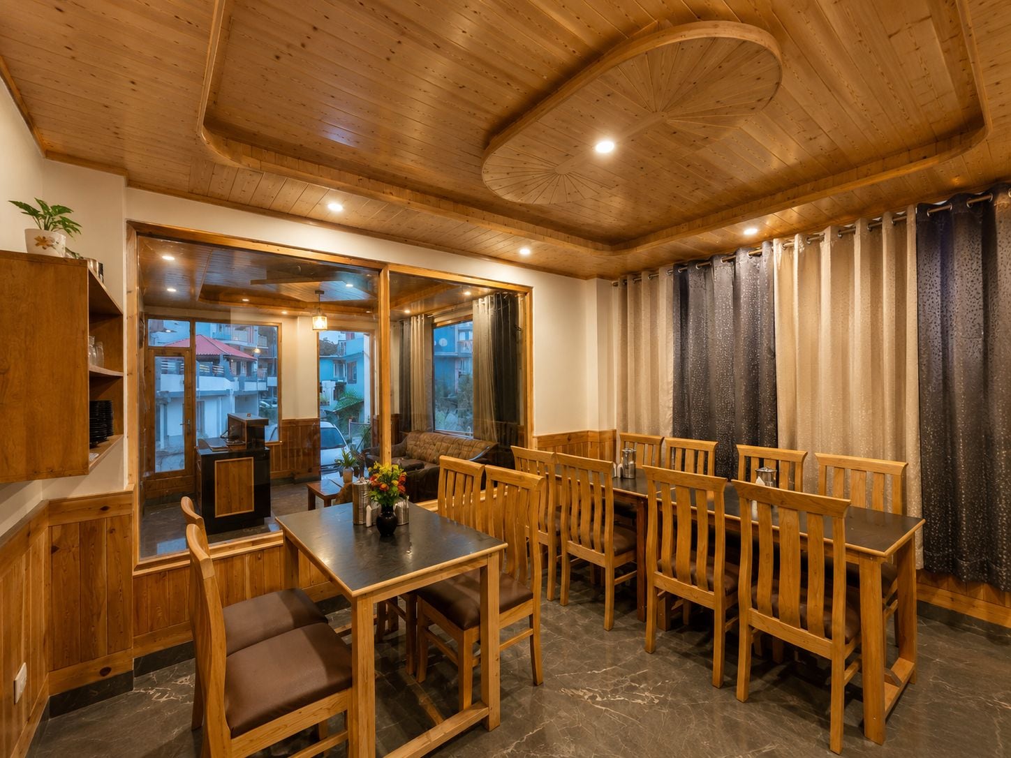 A wooden interior with a dining area featuring a table and chairs, a sofa, and a view through a glass door.