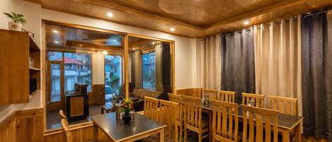 A wooden interior with a dining area featuring a table and chairs, a sofa, and a view through a glass door.