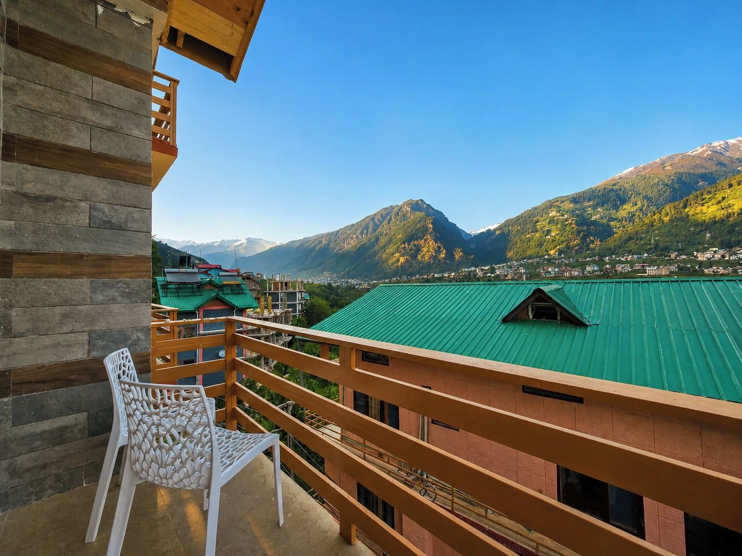 A balcony with a view of a mountain range and a green-roofed building.