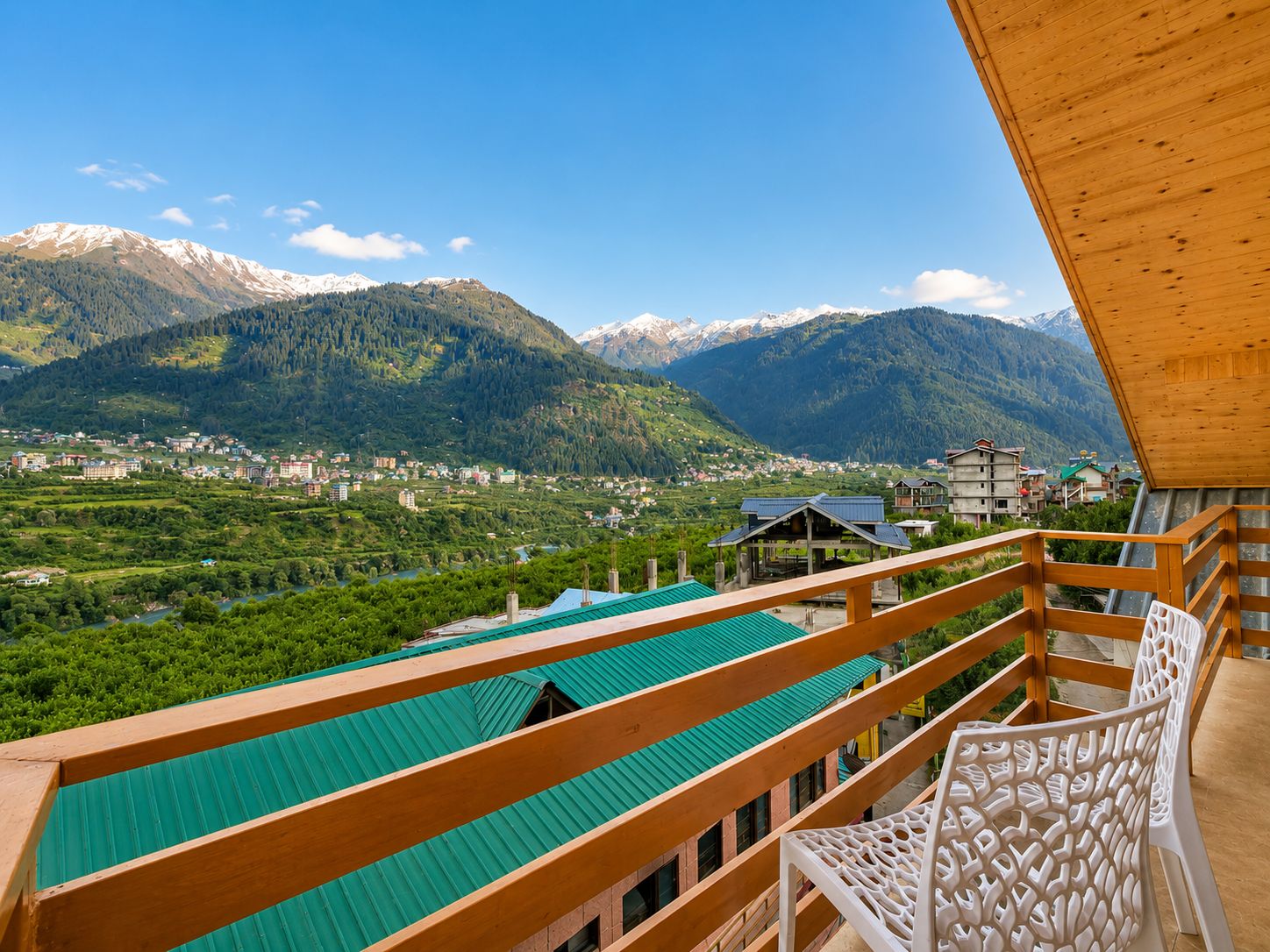 Un balcone con vista su un paesaggio montuoso, un edificio con tetto verde e una sedia bianca.