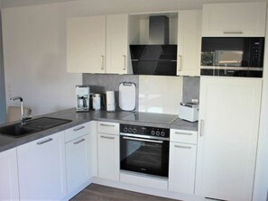 A modern kitchen with white cabinetry, a built-in oven, a microwave, and a coffee maker. - 50.4.s Waterkant (Wangerland)