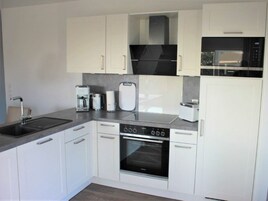 A modern kitchen with white cabinetry, a built-in oven, a microwave, and a coffee maker.