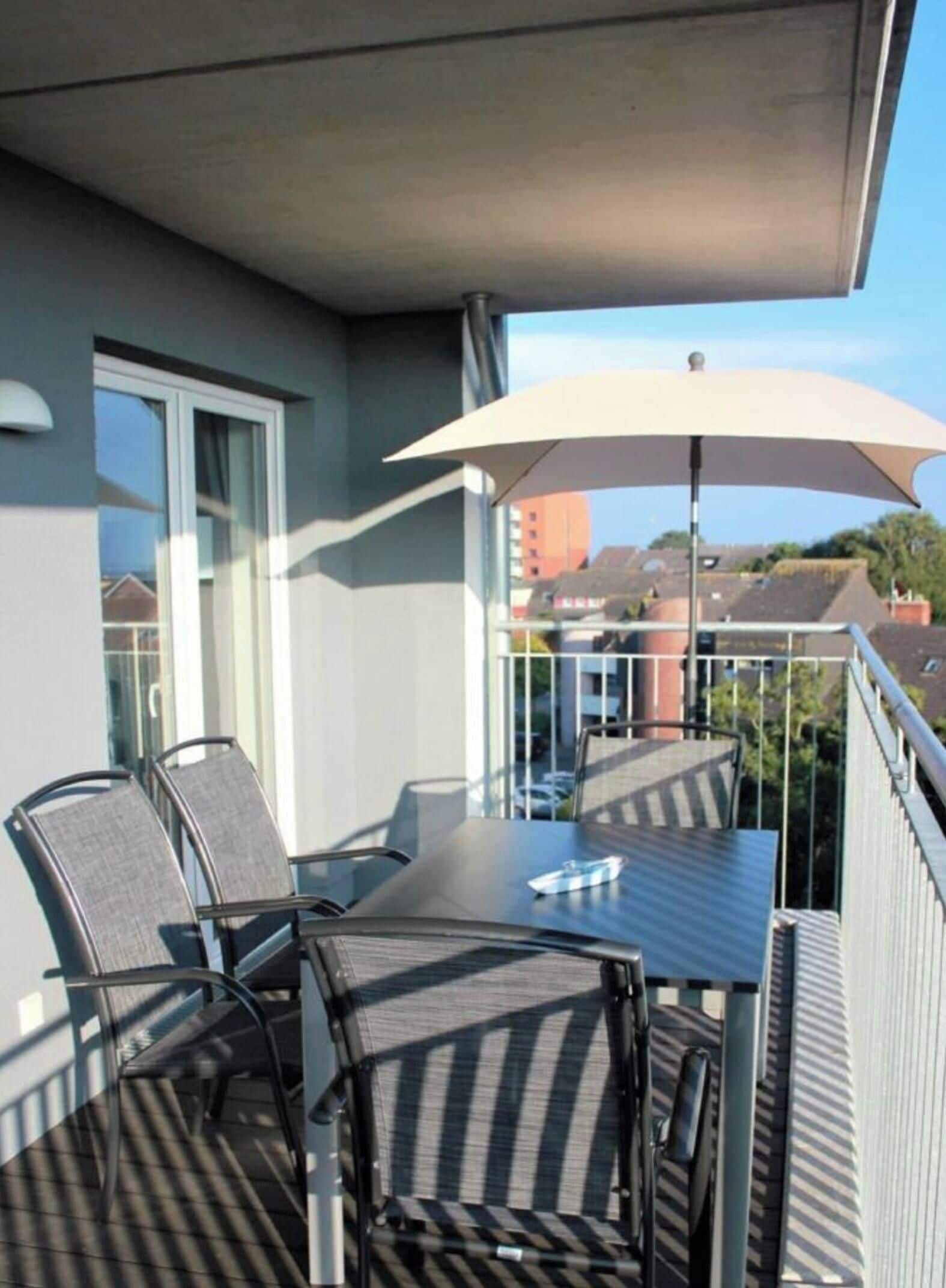 A balcony with a table and chairs, an umbrella, and a view of buildings in the background.