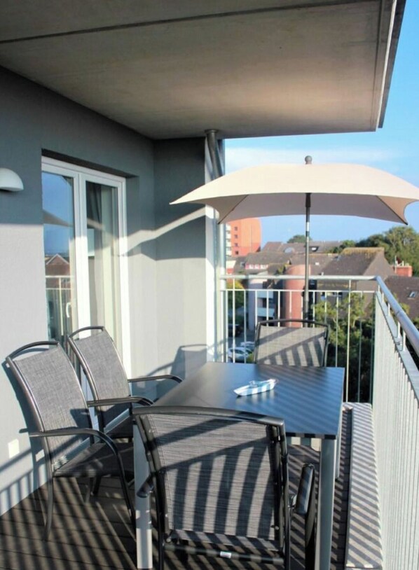 A balcony with a table and chairs, an umbrella, and a view of buildings in the background. - 50.4.s Waterkant (Wangerland)