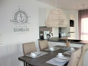 A modern dining area with a round table set for two, a decorative wall anchor graphic, and a hanging light fixture. - 50.4.s Waterkant (Wangerland)