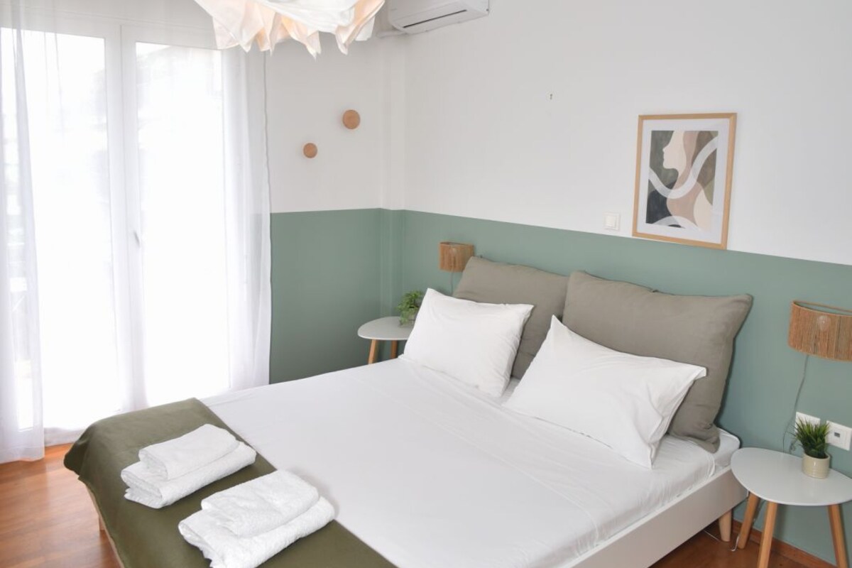 A bedroom with a bed, a bedside table, a hanging light fixture, and a wall-mounted air conditioner.
