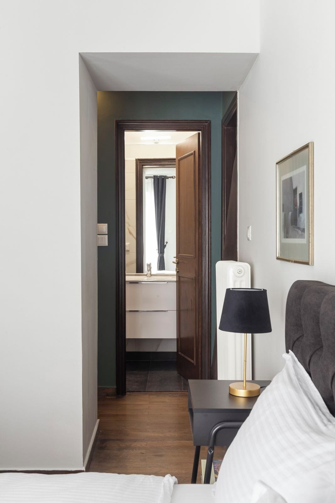Habitación de hotel con cama, escritorio con lámpara, espejo y vista al baño.