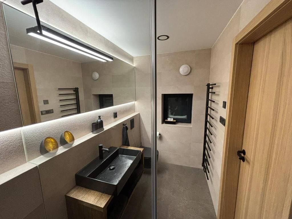 A modern bathroom with a glass partition, a black sink, and a wooden door.