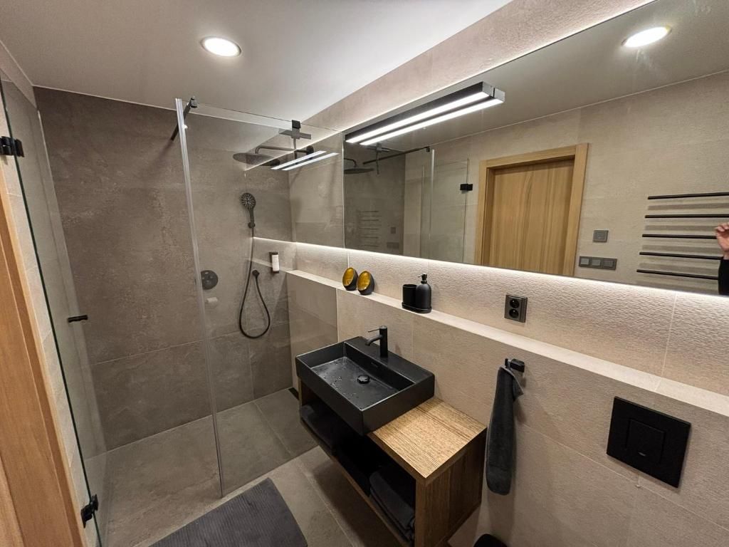 A modern bathroom with a glass-enclosed shower, a black sink, and a mirror with integrated lighting.