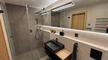 A modern bathroom with a glass-enclosed shower, a black sink, and a mirror with integrated lighting.