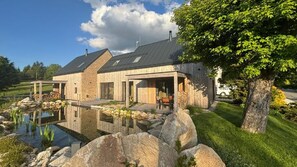 Una casa moderna con fachada de piedra, una amplia terraza y un estanque.