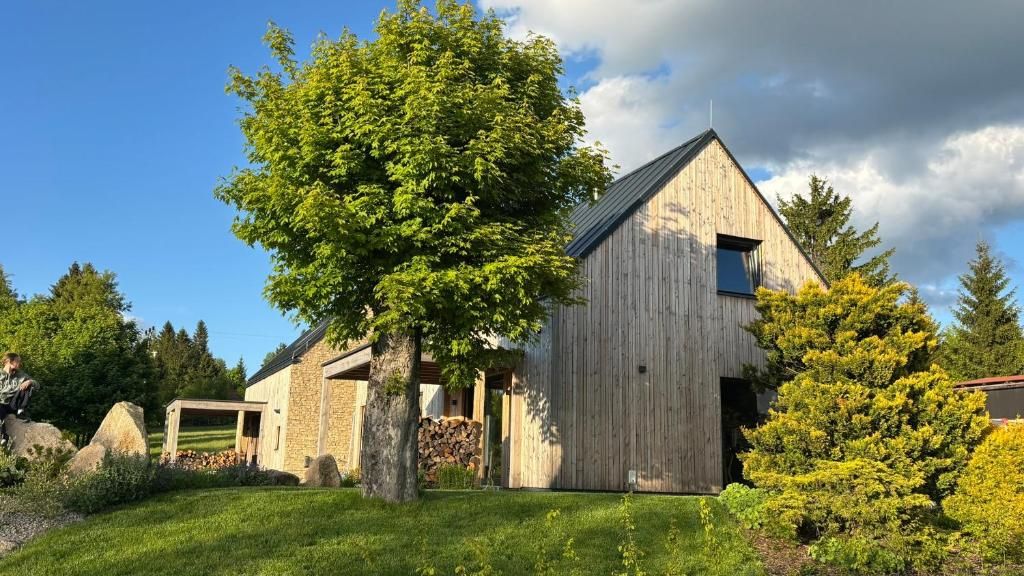 A wooden barn with a sloped roof, surrounded by a well-maintained garden with a large tree and shrubs.
