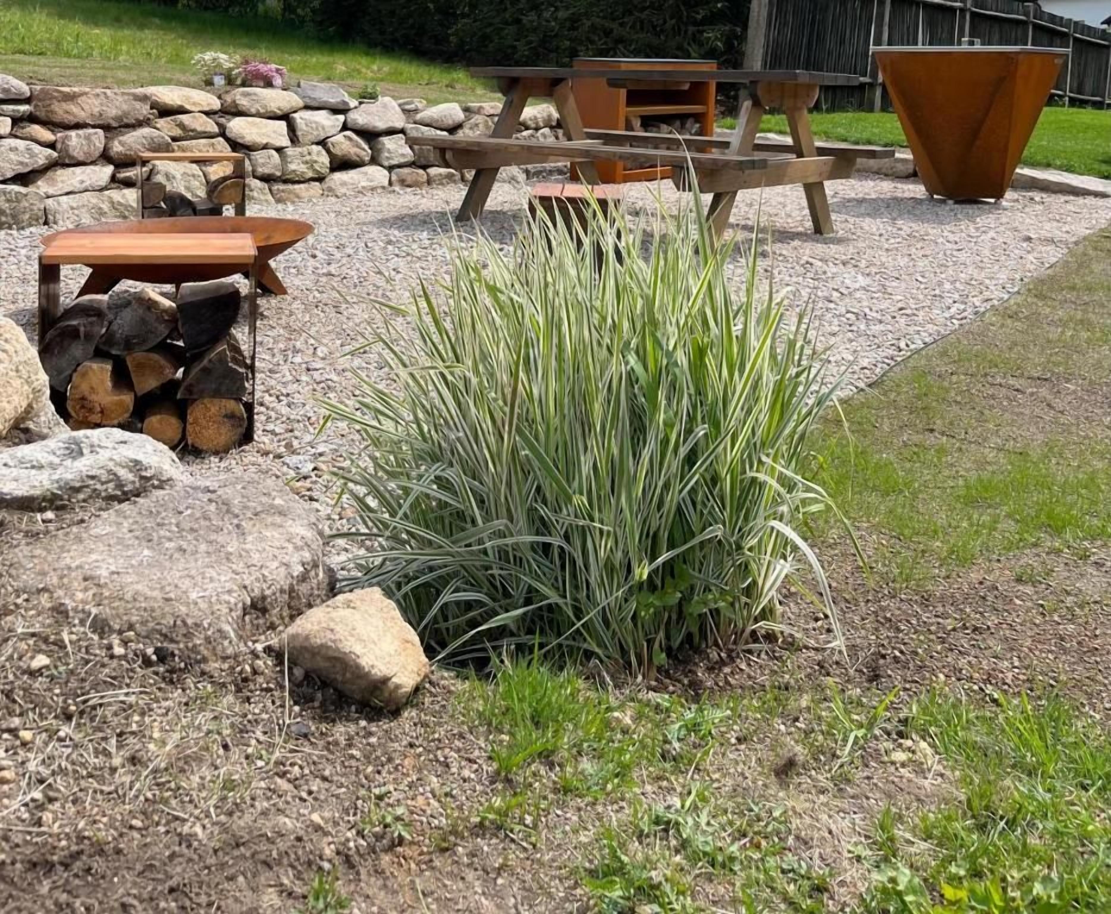 A garden area with a wooden table and chairs, a fire pit, and a pile of firewood.