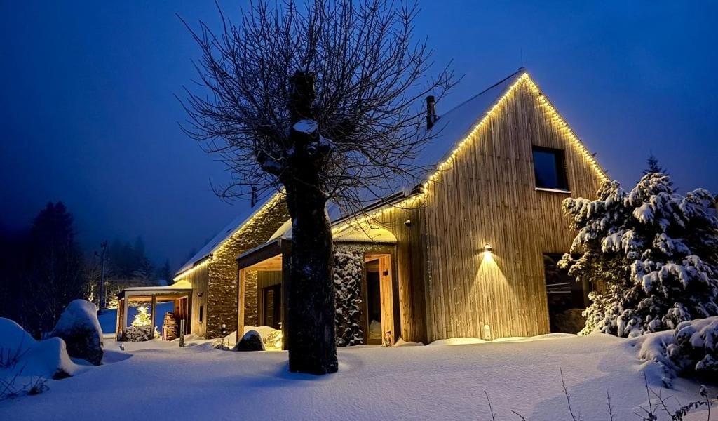Una cabaña de madera con techo inclinado, rodeada de nieve en el suelo y entre los árboles.